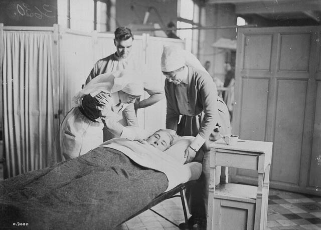 Wounded soldier in a bed being treated by nurses and doctor.