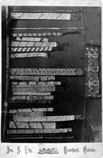 Black and white photograph of beaded belts of various sizes and designs, laying out on a surface for comparison
