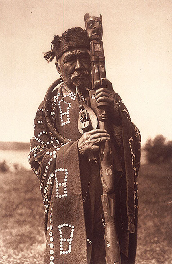 Sepia photograph of a man in ceremonial clothing, holding a carved staff